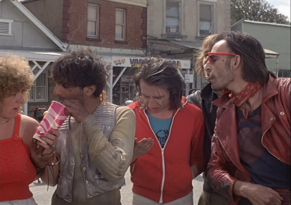 Ach, diese Glory Riders. Die "scharmante" Dame in Rot ist ne Tussi der Gang, mag Mudguts aber nicht wirklich, da er wieder wiederlich dreckig und unverschämt rüberkommt. Der junge Mann mit 70er Adidas-Jacke gefällt Cundalini und Diabando (der Typ hinten mit sehr gepflegten blonden Haar) nicht. Der arme Kerl wird verprügelt und anschließend am Motorrad angekettet quer durch das Dorf mit Vollgas gezogen.