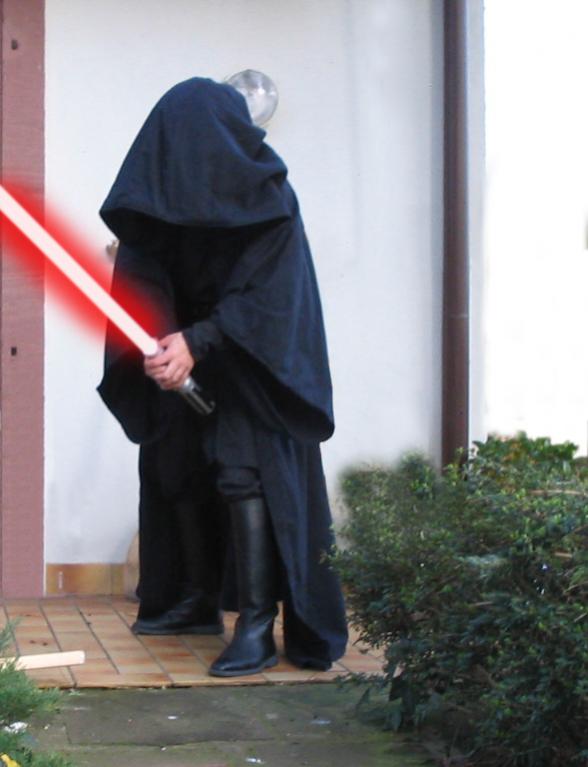 Mein Sith-Kostüm mit Anakin-Lichtschwert in rot (Photoshop, ich mag dich). Die Haube ist wirklich riesig und die gesammte Robe ist wirklich fast so tief wie in den Filmen. Zwei Zentimeter kürzer allerdings, weil mir der Verkäufer die Robe nicht so lang wie in den Filmen verkaufen wollte wegen seiner Versicherung, die es nicht erlaubt wegen der langen Robe im Treppenhaus zu stolpern und den Kunden das Genick dabei zu brechen. War einfach ein netter Kauf.